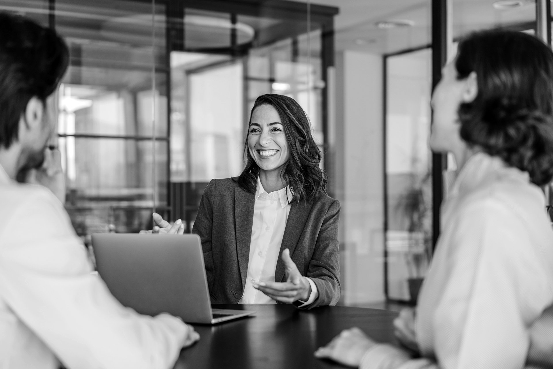 Lächelnde Beraterin erläutert Kund:innen im Meeting Qualitätssicherungslösungen im Bereich Software-Testing.